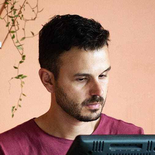 Retrato de Alex Cói, de perfil, trabalhando diante de um monitor
